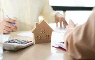Client signs a document to sell their home with a calculator and house figure on the table